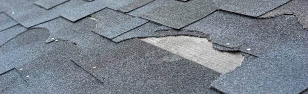 Сlose up view of asphalt shingles roof damage that needs repair.